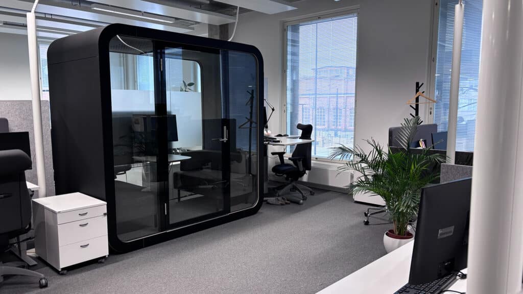 Vaalea toimistotila jossa harmaa kokolattiamatto ja erillinen äänieristetty työtilakoppi.