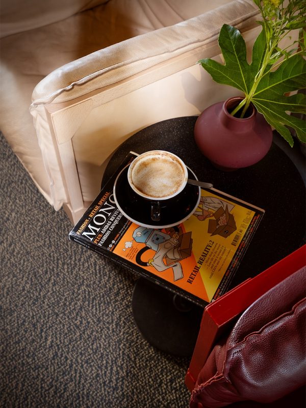 Vaalean nojatuolin vieressä on pöytä ja sen päällä Monocle-lehti, kahvikuppi ja viherkasvi.