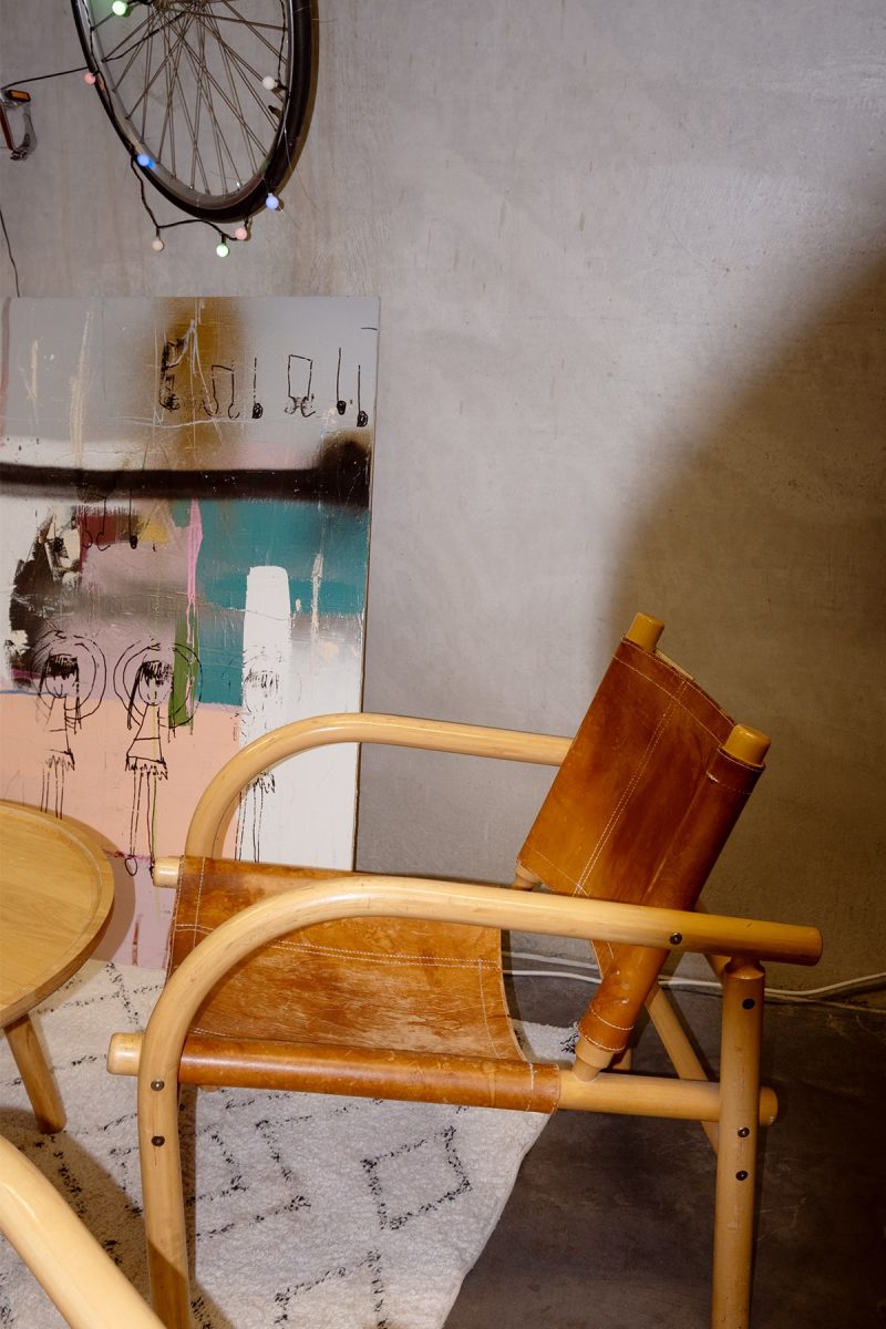 Taiteellinen ja retrohenkinen asetelma kuluneesta nahkatuolista, graafisesta taulusta ja polkupyörän renkaasta.